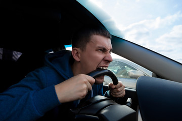 An emotional guy bites the steering wheel of a car while driving in a traffic jam on the road. Problems of big cities.