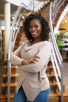 Beautiful African American woman posing at library. Front view of smiling lady with dreadlocks posing in front of stairs. Knowledge concept