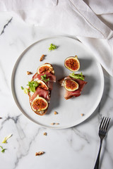 Trendy sandwiches with ham and figs on white plate and white marble patterned backgorund. Gourmet conception.