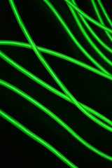 Toxic green luminous wires with different shapes and structures. A web of lime fiber and unusual circles located on a black glossy surface.