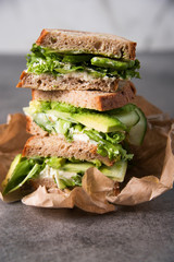 Three sandwiches on top of each other. Layered rustic breads with avocado and fresh salad on grey background.