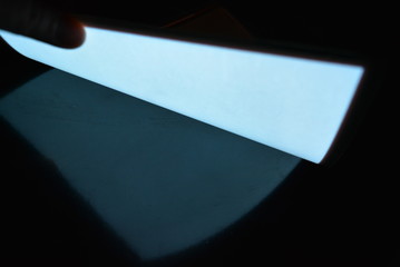 Very bright and luminous A4 electroluminescent paper with an  coating is located in different flatnesses on a pristine glossy surface with a female hand. Excellent color substrate, uniform glow.