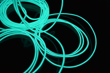 Unusual bright wires made of turquoise-colored material glowing at night. Chaotic sky blue wires, light guide electroluminescent wires, electroluminescence are located on a glossy black surface.