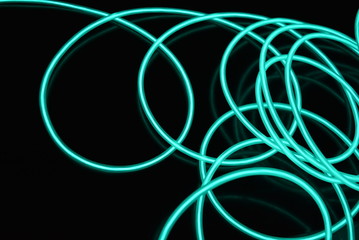 Unusual bright wires made of turquoise-colored material glowing at night. Chaotic sky blue wires, light guide electroluminescent wires, electroluminescence are located on a glossy black surface.