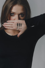 A crying young girl covering her mouth with her palm, on which there are three exclamation marks.