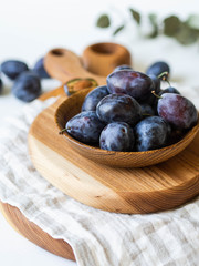 Blue ripe plums full wooden bowl on wooden board on a white background