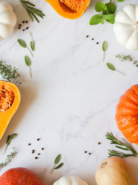 Pumpkins frame of various sizes and colors and different raw herbs and spices on marble background Top view. Copy space
