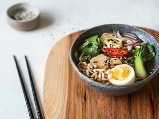 Asian Ramen noodles with chicken, pak choi cabbage and egg on wooden board on grey background