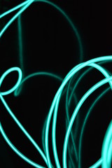 Unusual bright wires made of turquoise-colored material glowing at night. Chaotic sky blue wires, light guide electroluminescent wires, electroluminescence are located on a glossy black surface.