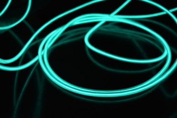 Unusual bright wires made of turquoise-colored material glowing at night. Chaotic sky blue wires, light guide electroluminescent wires, electroluminescence are located on a glossy black surface.