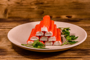 Ceramic plate with pile of crab sticks and parsley twig on a wooden table