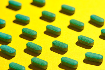 Obraz na płótnie Canvas medicinal capsules, pills and tablets on yellow background. nutrition supplements, green vitamin pills. pills pattern on a yellow background