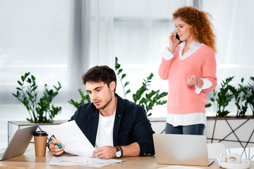 selective focus of man doing paperwork and woman talking on smartphone in office