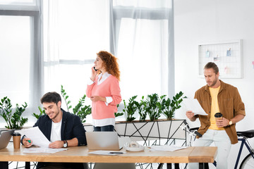 three friends doing paperwork and talking on smartphone in office