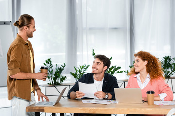three smiling friends doing paperwork and talking in office