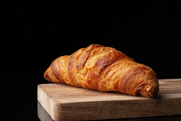 Classic french croissant on a wooden board. Black background. Cutting board. Homemade baking.
