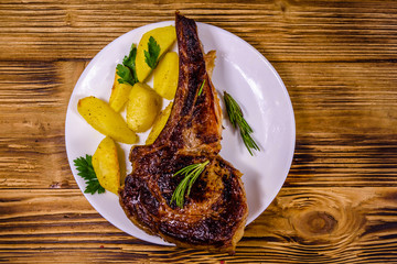 Plate with roasted ribeye steak on wooden table. Top view
