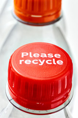 Plastic bottles and orange and red bottle caps with please recycle message against a white background. Concept of plastic pollution. Vertical image.