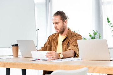 handsome man doing paperwork and looking at laptop