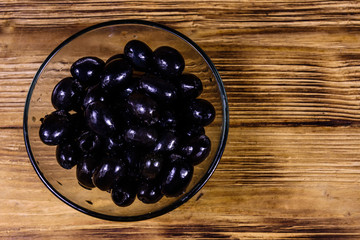 Glass bowl with black olives on wooden table. Top view