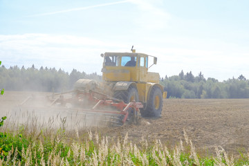A farm tractor cultivates land after harvesting grain.