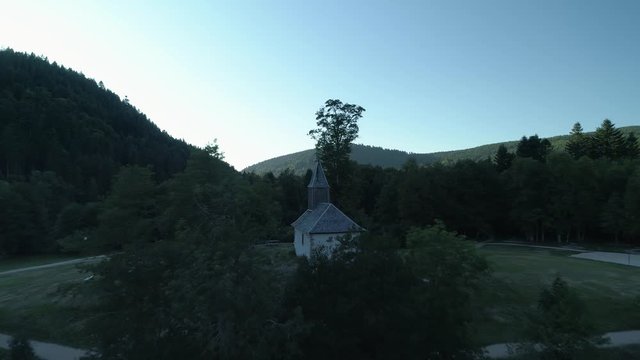 A pushback droneshot of a little church shows the whole area of a lake at sunset