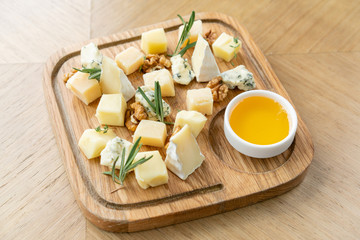 Cheese plate. Delicious cheese mix with walnuts, honey on wooden table. Tasting dish on a wooden plate. Food for wine.