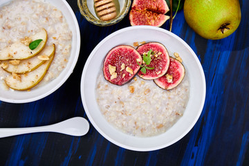 A bowl of porridge with pears slices and walnuts and porridge with figs on dark blue background. Two bowls. Flat lay. Copy space. Top view.