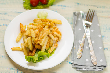 French fries with meat on a white plate on a wooden light background.