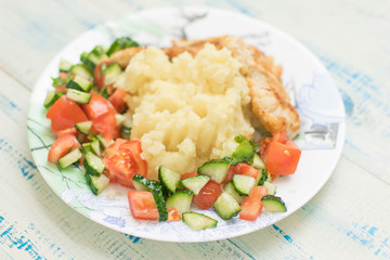 Mashed potatoes with chop and fresh vegetable salad in a plate on wooden background.