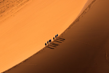 Aerial view group of people walking on the sand dune in the desert and sun gradually create beautiful scene. - obrazy, fototapety, plakaty