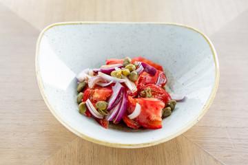 Salad of colorful tomatoes, olives, capers and basil. Wooden table in restaurant