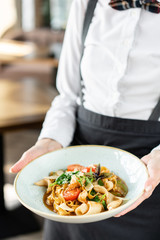 The waiter is holding a plate Italian pasta tagliatelle with seafood and tomato sauce. Pasta Gamberini. Restaurant menu