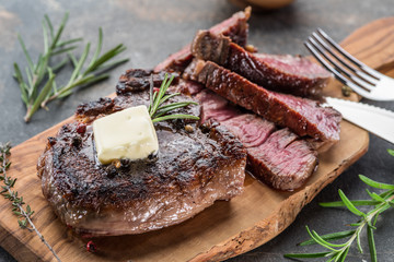 Medium rare Ribeye steak with herbs and a piece of butter on the wooden tray.