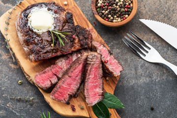 Medium rare Ribeye steak with herbs and a piece of butter on the wooden tray.