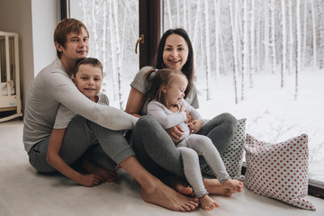 The family is sitting at the window and looking at the winter forest. Good New Year spirit. Morning in pajamas.