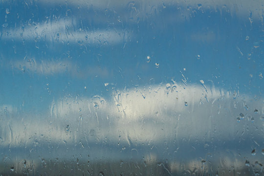 beautiful clouds and city behind wet rainy glass with droplets