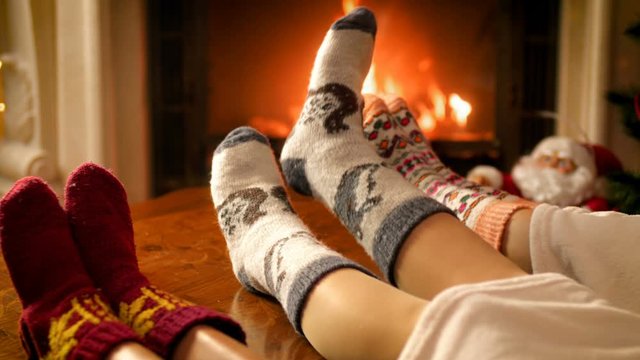 Closeup 4k video of family lying under blanket wearing warm woolen socks warming by the fire in fireplace. People relaxing on winter holidays and celebrations at home