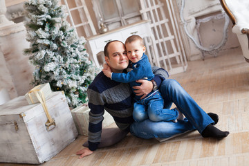 Cheerful bald dad with his son in sweaters waiting for the New Year against the background of the Christmas Tree.