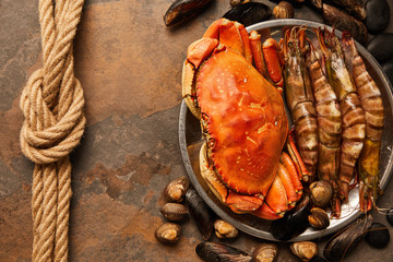 top view of uncooked crab, shellfish, cockles and mussels in bowl near rope on textured surface