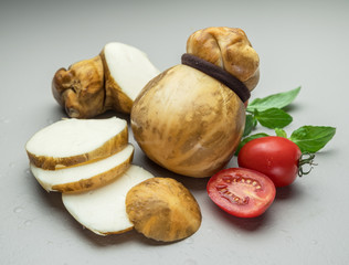 Traditional Italian smoked Scamorza cheese with herbs and tomatoes on gray background.