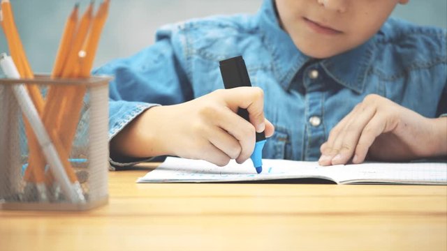 Hands of little schoolboy drawing in his copybook with blue highlighter. Blurred forefront, moving video.