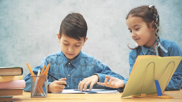 Concentrated schoolboy is highlighting something with the ruler, then his sister is coming, wanting to take the ruler, looking with lovely face expression, but brother makes her go away.