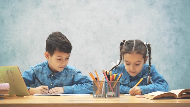 Schoolkids doing their homework, brother is writing off of his sister. Sister is looking at him conspiciously.