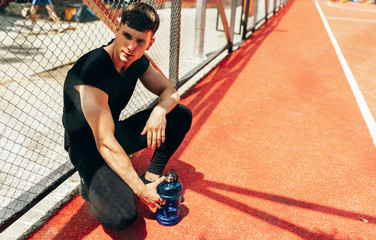 Image of handsome fit young man resting after workout, with a bottle of water on black background. Healthy male taking a break after exercising outdoors.