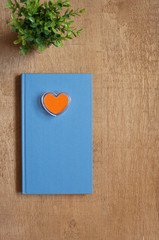 Flat layout of a blue book and orange heart stamp on wooden desk background.