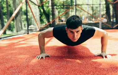 Outdoors image of young muscular man doing push-ups on workout ground. Caucasian fitness male doing workout exercises on sunset light background. People and sport concept