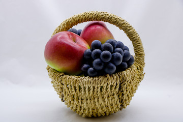 Apples and grapes in a basket on a white background.