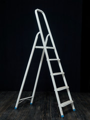 White metal stepladder on a black background.