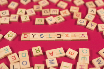high angle view of a wooden alphabet blocks with DYSLEXIA word in the center on pink background. Concept of Dyslexia awareness and human brain development - obrazy, fototapety, plakaty